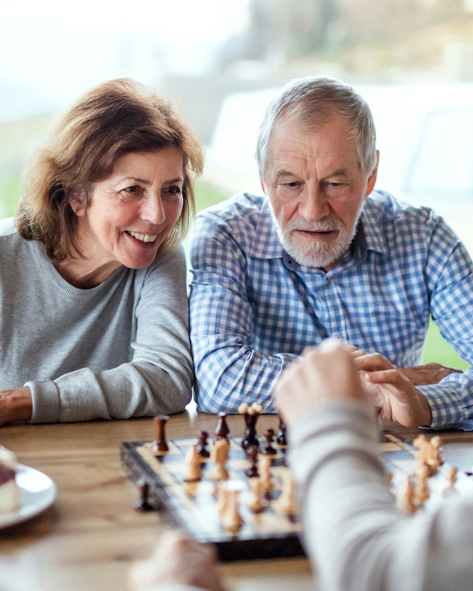 Two older adults smile and talk across a chessboard during a game.